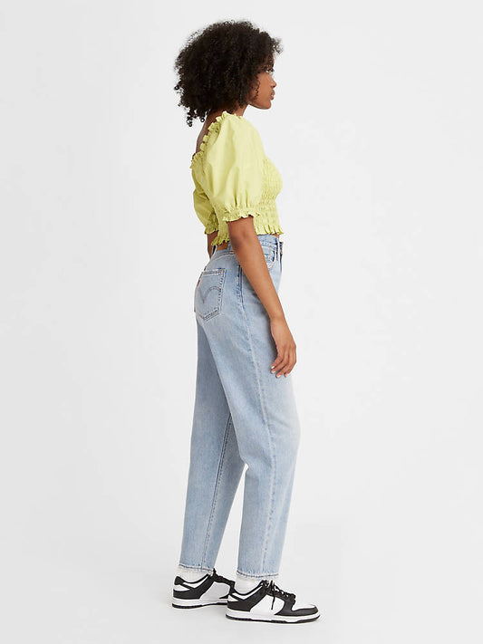 Women is wearing Levi's high loose tapper fit jeans. These Jeans are light blue color, high waistes and ripped. Jeans are paired with light green cropped top and black sneakers. The photo is taken from the side. (7721828384976)
