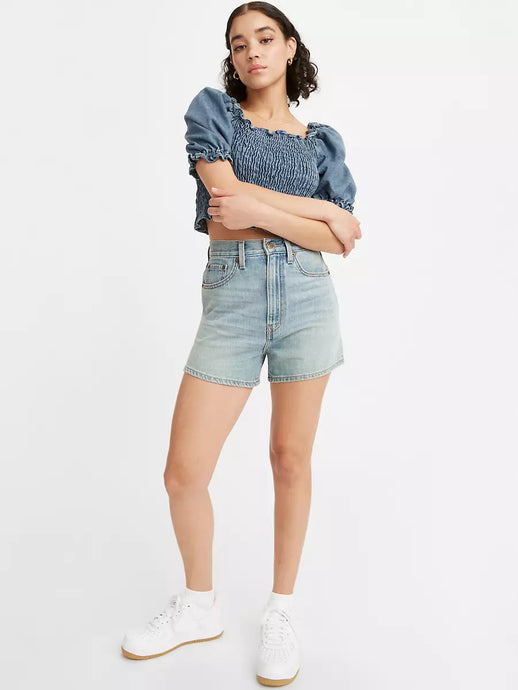 Woman is wearing Levi's high loose shorts. Jean shorts feature high waist and vintage inspired relaxed fit. Jean shorts are paired with dark denim top and white sneakers. (7721844474064)