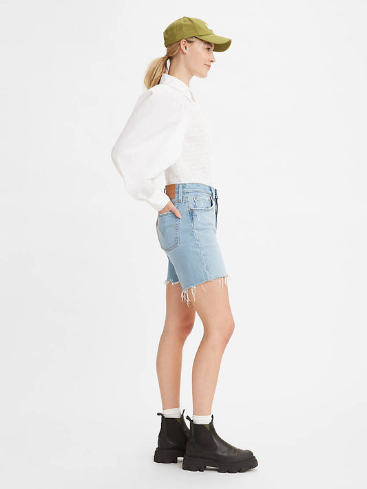 Women is wearing Levi's 501 original mid thigh shorts in light wash color. Jean shorts are styled witha white shirt and black boots. Jean shorts feature high waist, bermuda lenght and classic straight fit. The photo demostrates jean shorts from the side. (7721852010704)
