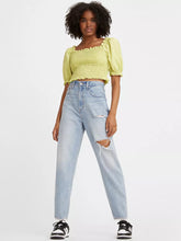 Load image into Gallery viewer, Women is wearing Levi&#39;s high loose tapper fit jeans. These Jeans are light blue color, high waistes and ripped. Jeans are paired with light green cropped top and black sneakers. (7721828384976)
