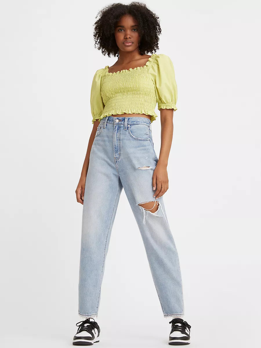 Women is wearing Levi's high loose tapper fit jeans. These Jeans are light blue color, high waistes and ripped. Jeans are paired with light green cropped top and black sneakers. (7721828384976)