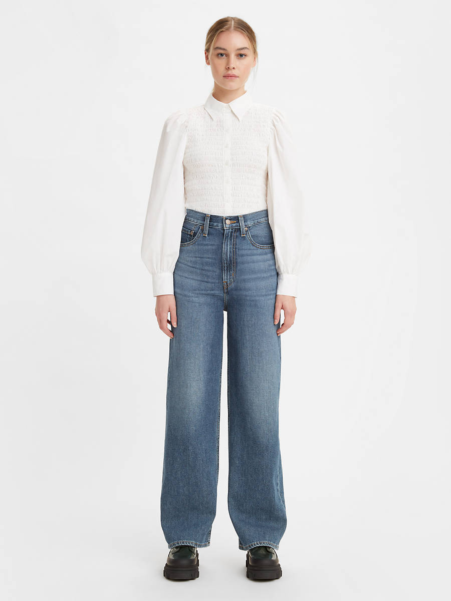 Women is wearing Levi's High Loose Jeans in dark denim. Jeans feature high waist, five pockets wide leg fit and full length. Jeans are paired with black loffers and white blouse. (7721847947472)