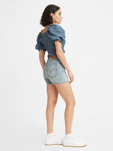 Load image into Gallery viewer, Woman is wearing Levi&#39;s high loose shorts. Jean shorts feature high waist and vintage inspired relaxed fit. Jean shorts are paired with dark denim top and white sneakers. The photo demonstrates the outfit from the side. (7721844474064)
