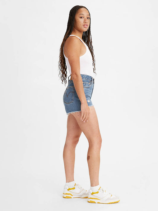 Woman is wearing Levi's ribcage shorts. Denim shorts feature flattering high waist, slightly loose fit and chewed hem. Denim shorts are paired with a white top, light denim striped jacket and white sneakers. The photo demonstrates the model from the side. (7721844310224)