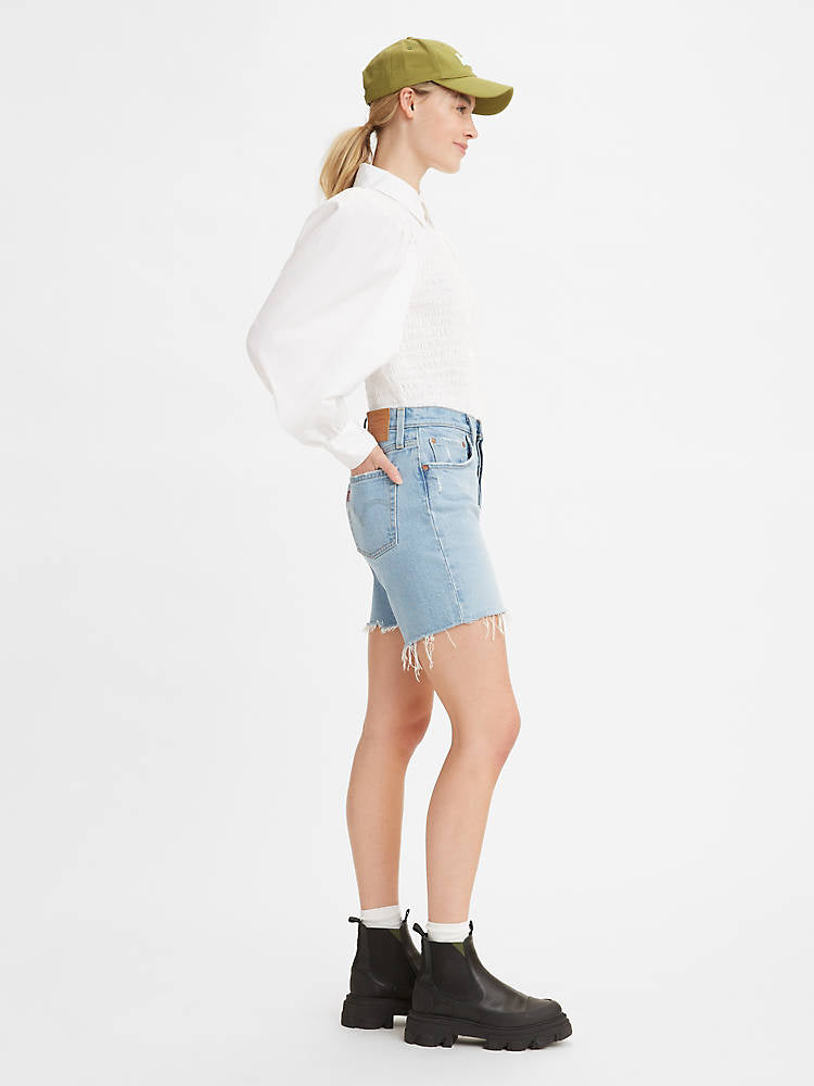 Women is wearing Levi's 501 original mid thigh shorts in light wash color. Jean shorts are styled witha white shirt and black boots. Jean shorts feature high waist, bermuda lenght and classic straight fit. The photo demostrates jean shorts from the side. (7721852010704)
