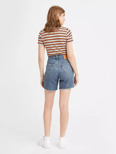Load image into Gallery viewer, Woman is wearing Levi&#39;s mid thigh shorts. Jean shorts feature high waist, mid thigh length and cut off hem. The photo demonstrates the model from the back (7721825140944)
