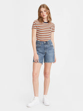 Load image into Gallery viewer, Woman is wearing Levi&#39;s mid thigh shorts. Jean shorts feature high waist, mid thigh length and cut off hem. Shorts are paired with a stripped T-shirt. (7721825140944)
