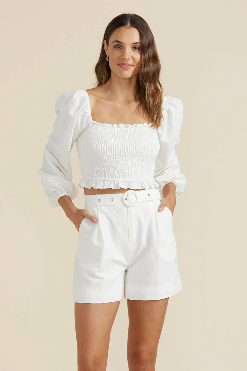 Woman is wearing ivory Minkpink azalea crop top with puffed sleeves and elastic body. the top has ruffle detail on waist and a square neck. The top is paired with Azalea belted shorts that are fitted and have two side pockets. (7714613231824)