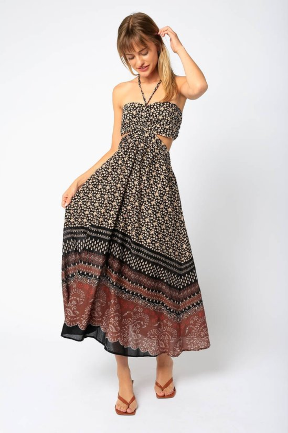 Woman is wearing Olivaceous Halter Maxi Dress.  The Maxi dress features cutouts and open back. The dress is black color with various prints in beige and red colors. (7706621706448)