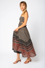 Load image into Gallery viewer, Woman is wearing Olivaceous Halter Maxi Dress.  The Maxi dress features cutouts and open back. The dress is black color with various prints in beige and red colors. The photo demostrates the model from the side. (7706621706448)
